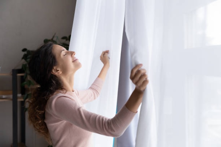 mujer que abre las cortina tomando aire
